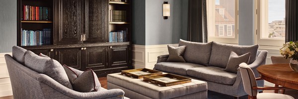 Refined living space with tailored blue seating, a central ottoman, and dark wood cabinetry filled with books.