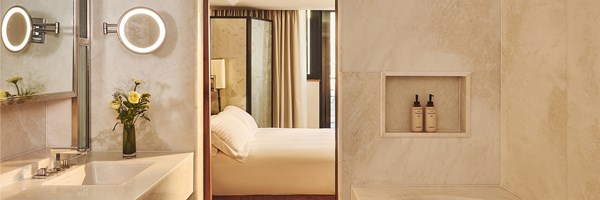 Bright studio bedroom with tall windows, a blue curved sofa and round table beside neutral drapes