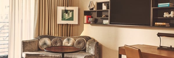 Velvet sofa with round cushions beside a wall-mounted TV and desk under tall curtains