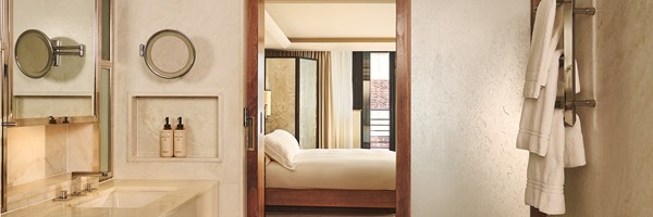 Marble bathroom with vanity and robes, looking through a doorway to a softly lit bed
