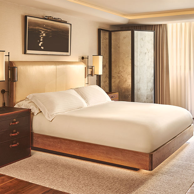 Bright bedroom with a padded headboard, marble screen and soft lighting beside tall curtains.