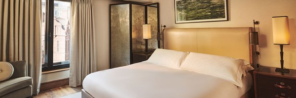 Bedroom with a large bed, mirrored screen and window offering views of historic buildings