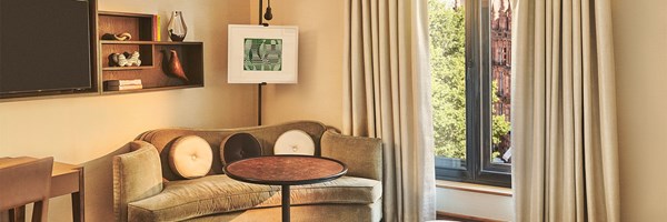 Cosy seating area with curved sofa, round table and artwork beside a window with draped curtains.”