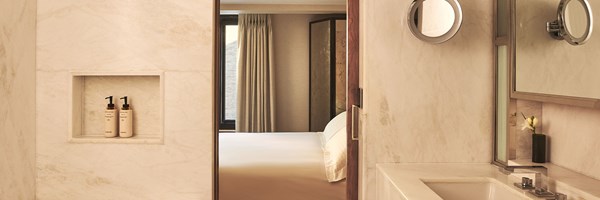 Marble bathroom with built-in toiletries, looking through to a softly lit bedroom with neutral décor.
