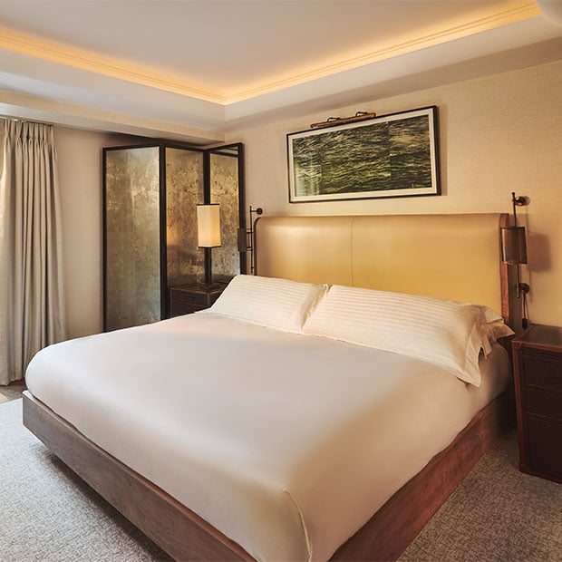 Contemporary bedroom with a large bed, leather headboard and soft lighting beside a mirrored screen