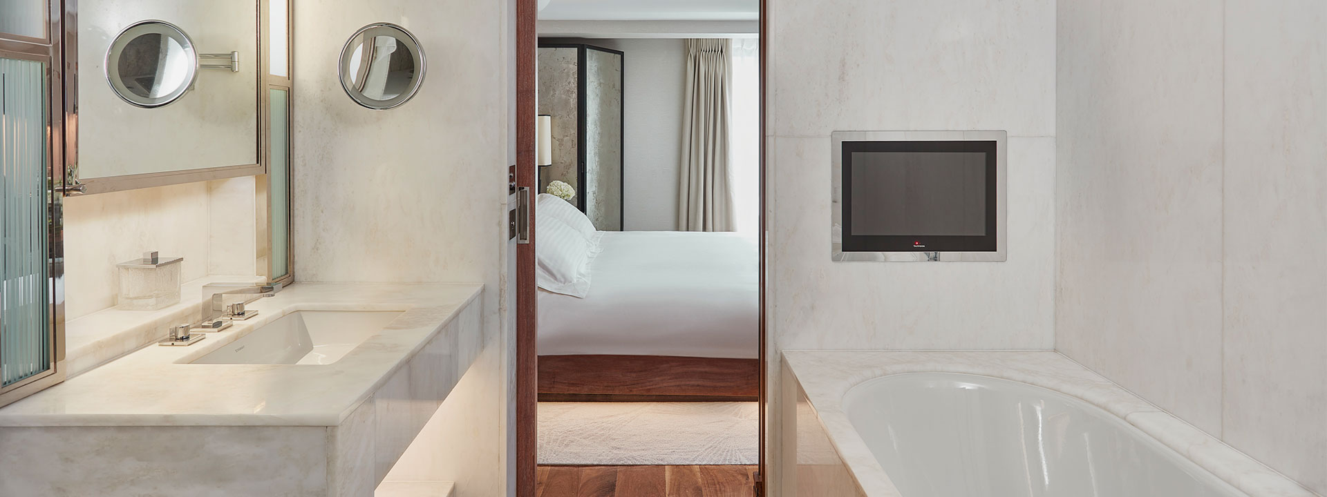 View from marble ensuite bathroom with bathtub TV in Contemporary Superior Room, towards the bedroom.