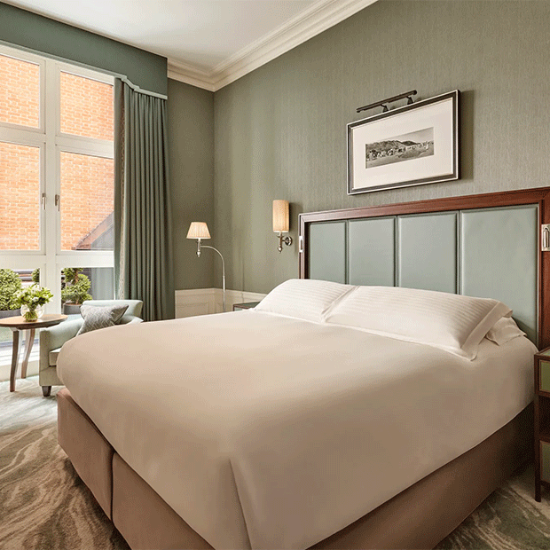 Superior hotel bedroom with a king-size bed, green upholstered headboard, framed artwork and tall windows overlooking a courtyard.