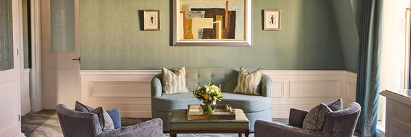 A sitting area with a curved sofa, two armchairs and a coffee table, set against green walls and artwork.