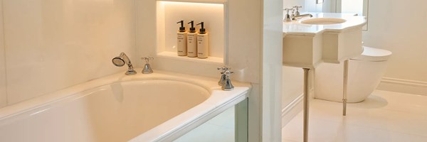A bright bathroom with a built-in bathtub, chrome taps and toiletries set in a lit wall niche.