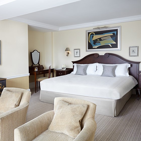 Classic interior in the bedroom of the Deluxe Junior Suite, with a view of the King Bed and armchairs.