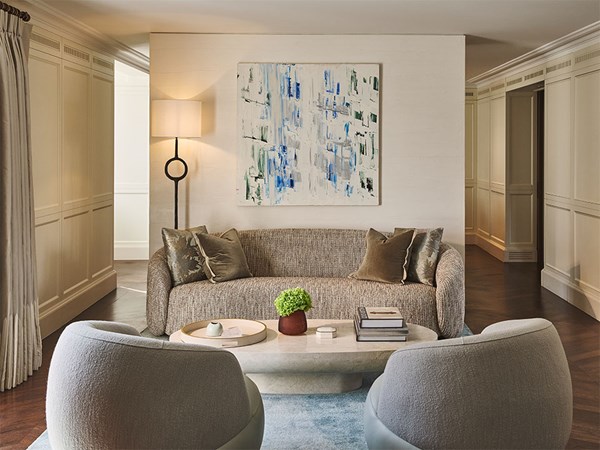A cosy sitting area with a curved grey sofa, two rounded armchairs, a low oval coffee table, and an abstract blue and white painting on the wall behind.