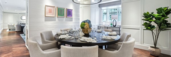 Elegant dining room with circular table set for eight, floral centrepiece, and views into the lounge with wood flooring.