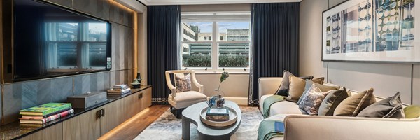 Stylish media room featuring a wall-mounted TV, plush seating, bookshelves, and city views through large double windows.