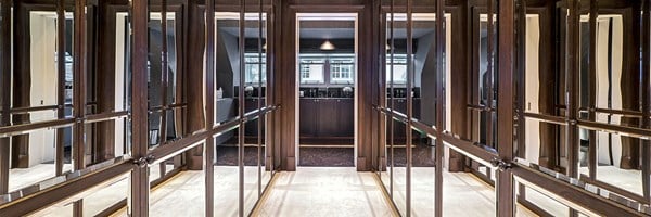 Spacious walk-in wardrobe with mirrored dark wood cabinetry, cream carpet, and direct access to double-vanity en suite bathroom.