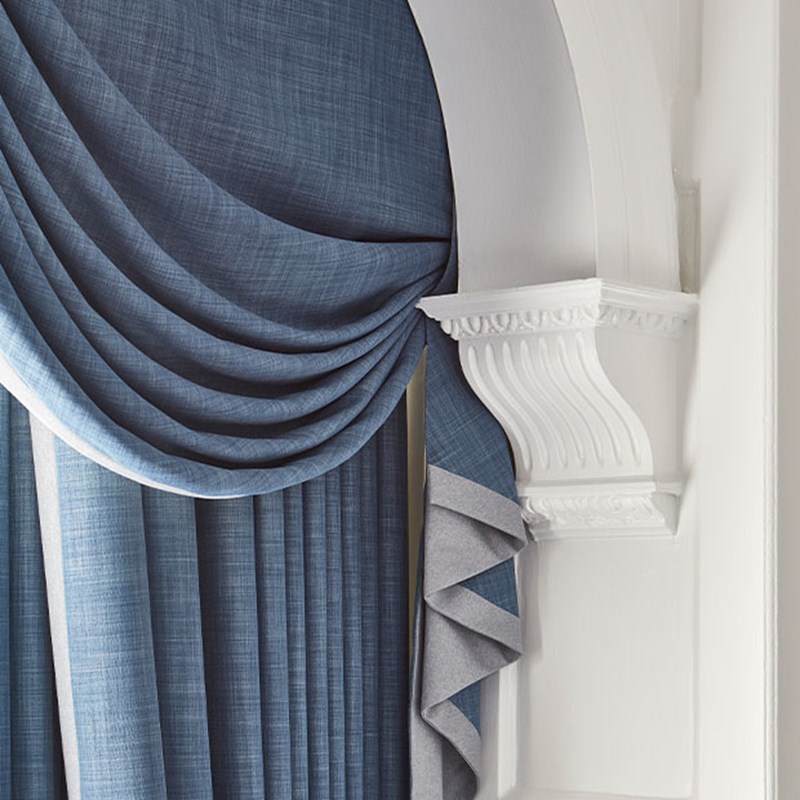 Luxurious blue curtains draped elegantly beside an intricately carved white column, creating a timeless and refined look.