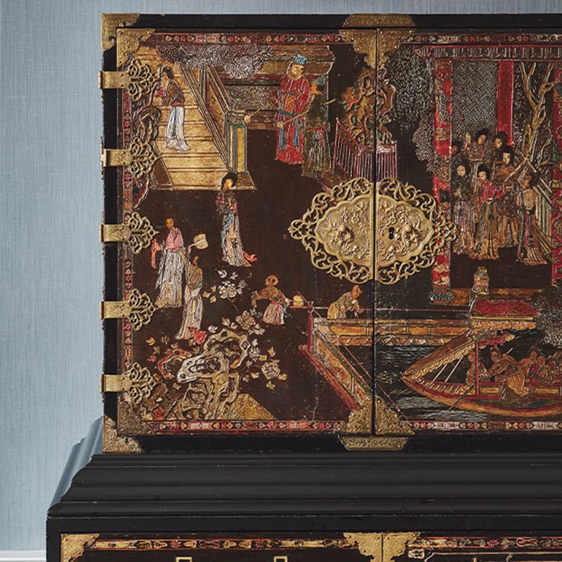 An ornate lacquered cabinet adorned with intricate Asian-style gold detailing and hand-painted figures, adding a touch of global sophistication.