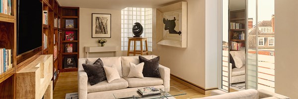 efined lounge with cream sofas, wood panelled bookshelves, modern artwork, and large glass doors leading to a private balcony overlooking rooftops.