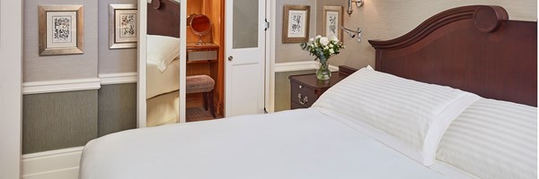 king sized bed with wooden headboard, wooden side table with a vase of flowers, view into dressing room