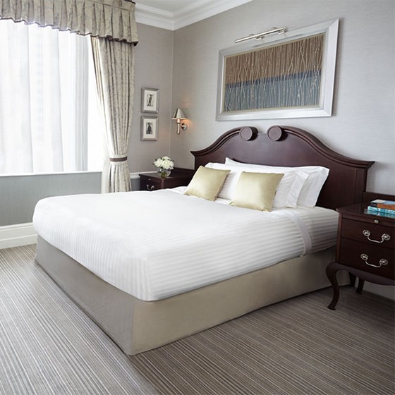 Superior Single Room: Queen sized bed with dark wooden headboard, a wooden desk with a blue cover and a vase of flowers sits in front, with a blue chair tucked behind the desk.