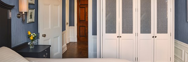 A bedroom corner with white paneled doors, blue walls and a bedside table with yellow flowers.