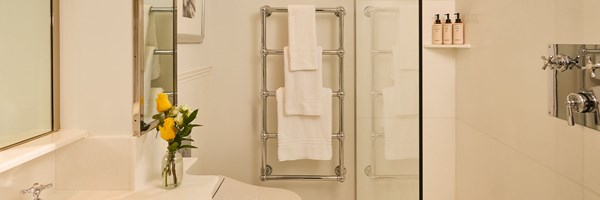 A bright bathroom with white tiles, a towel rail and a small vase of yellow flowers by the sink.