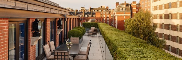 Spacious private terrace at The Connaught’s Terrace Suite, featuring elegant outdoor seating, manicured hedges, and views of classic red-brick Mayfair architecture at golden hour.