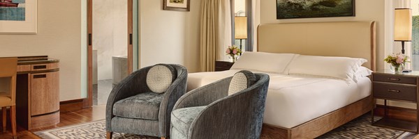Refined bedroom in The Connaught’s Terrace Suite, showcasing a king-size bed with crisp white linens, two plush armchairs, and soft natural light from large windows.