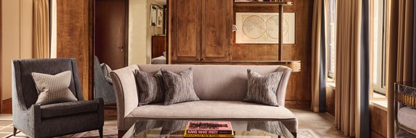 Sophisticated living room in The Connaught’s Terrace Suite, with a soft neutral-toned sofa, armchair, and bespoke wooden cabinetry adorned with curated books and artwork.