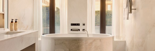 Serene bathroom in The Connaught’s Terrace Suite, featuring a freestanding marble bathtub, dual vanity, and floor-to-ceiling windows framed by sheer curtains.