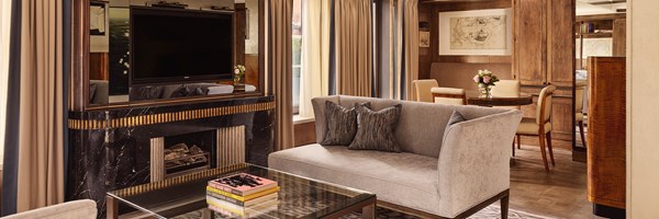 Elegant living room with a modern fireplace, flat-screen TV, gray sofa, glass coffee table, and soft natural lighting
