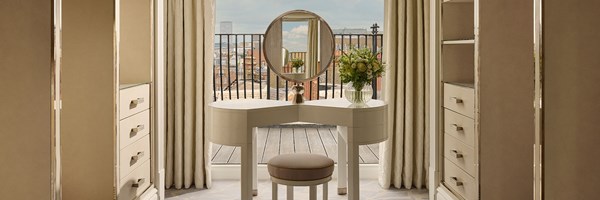 Elegant dressing space featuring a sculptural vanity and circular mirror, framed by mirrored wardrobes and opening to a rooftop terrace.
