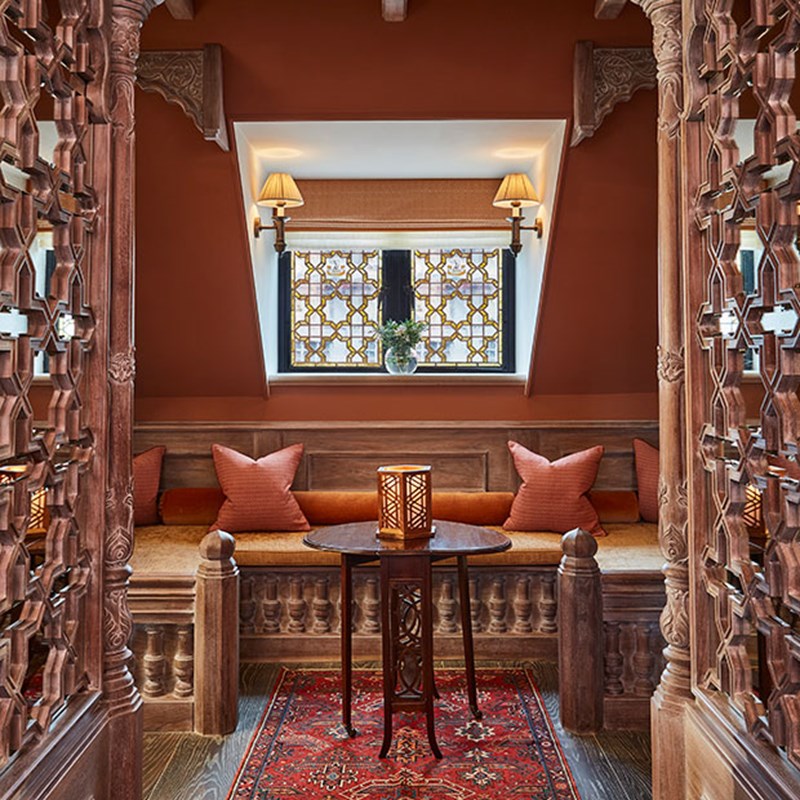 The King's Lodge at The Connaught. Looking through the wooden architecture onto a seating area with a table and candle placed on it, with pillows on the sofa and a stain glass window behind