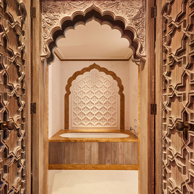 Ornate bathroom with a carved arch framing a marble alcove and a round soaking tub below.
