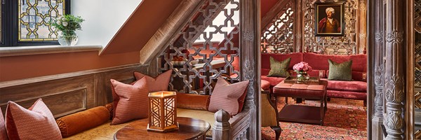Cosy lounge with carved wood screens, red sofas and patterned cushions under a sloped ceiling
