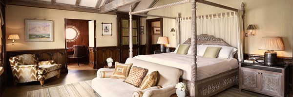 Spacious suite with a carved four-poster bed, seating area and study nook with a porthole window.