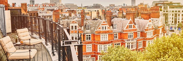 Balcony with cushioned chairs overlooking red-brick rooftops and London’s skyline.