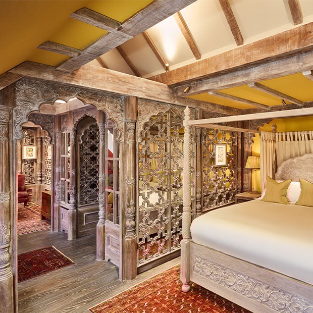 Suite with a carved four-poster bed and intricate wood screens under exposed beams and warm lighting.
