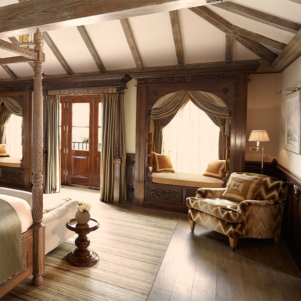 Spacious bedroom with carved wood window seats, neutral tones and timber ceiling beams
