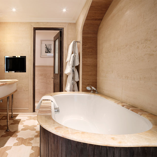 Light marble bathroom with a deep oval tub, robes on a heated rail and dual mirrors above the sink.