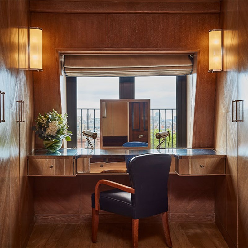 Elegant dressing table with a leather chair, twin makeup lights, and a central mirror positioned in front of a large window offering expansive views across the London skyline.
