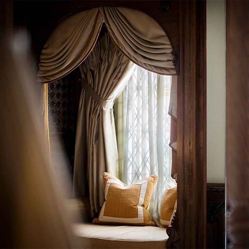 Elegant alcove with a canopied window seat dressed in golden cushions and draped curtains, filtered natural light creating a calm and intimate setting.