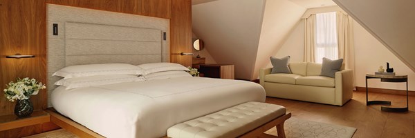 Serene attic-style bedroom with a textured headboard, soft cream furnishings, and natural wood accents beneath sloping ceilings.