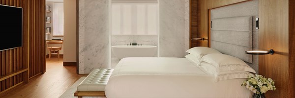 Light-filled bedroom with wood paneling and a view into a sleek marble bathroom featuring a freestanding tub.