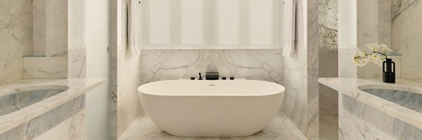 Minimalist bathroom wrapped in white-veined marble, centred around a sculptural standalone bathtub beneath frosted windows.