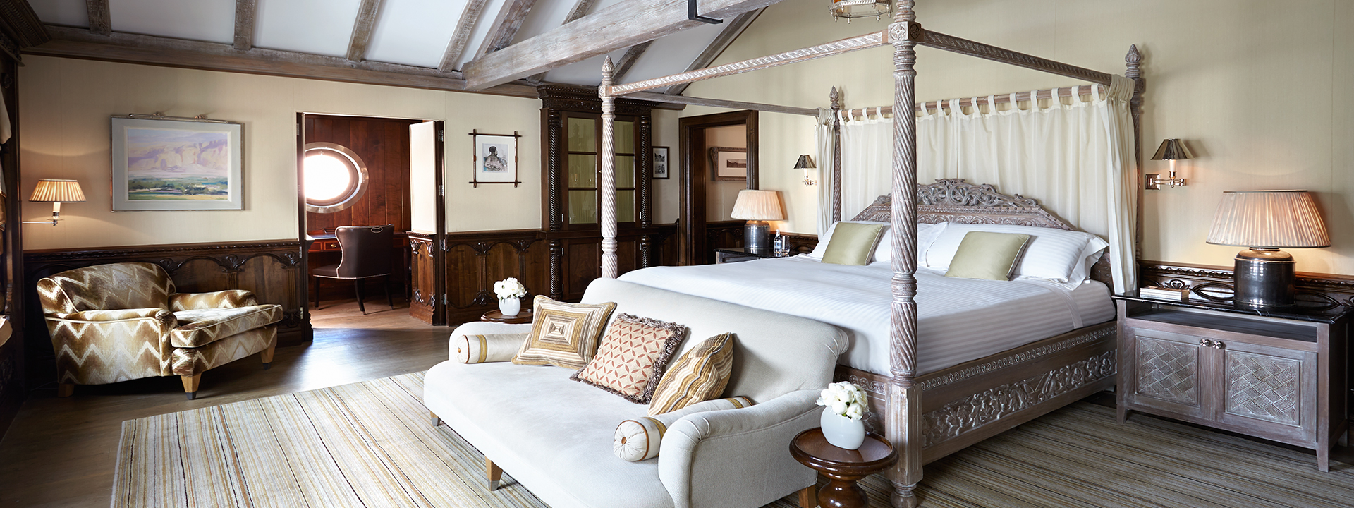 Comfortable and spacious four poster bed 
with a beige wall and wooden furniture in the Princes Lodge Room.