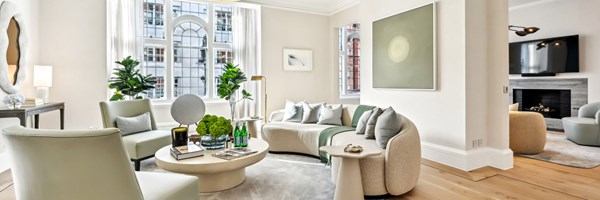 Bright living room with curved sofa, soft green accents, statement art, and arched windows overlooking Mayfair architecture.
