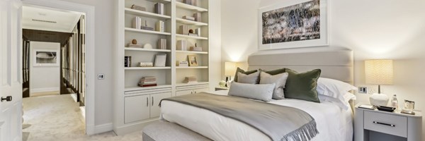 Elegant bedroom featuring built-in bookshelves, neutral tones, and plush bedding, with view through to mirrored dressing area.
