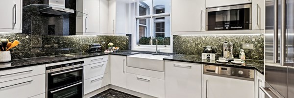 Modern kitchen with glossy white cabinetry, black marble countertops, and stainless steel appliances beneath a bright sash window.