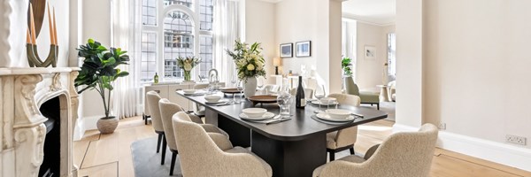 Sophisticated dining room with dark wood table, cream chairs, marble fireplace, and arched windows flooding the space with light.