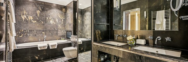 Luxurious bathroom in polished marble with double sinks, soaking tub, walk-in shower, and ambient lighting.